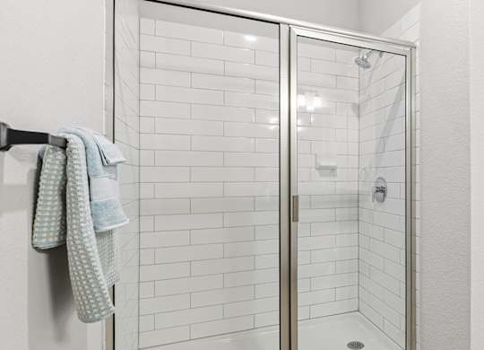 A white tiled shower with a glass door and a towel hanging on the wall.
