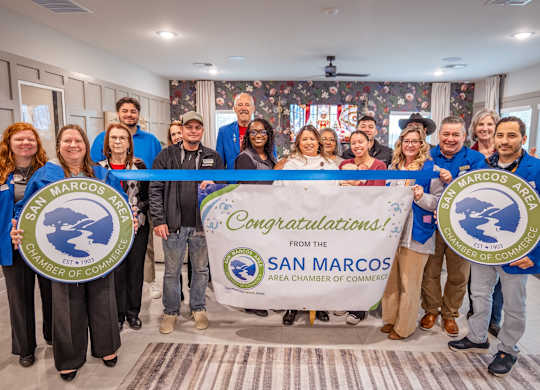 A group of people are holding a banner that says "Congratulations! From the San Marcos Area Chamber of Commerce".