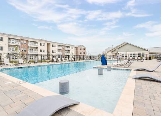A large outdoor swimming pool with lounge chairs and a building in the background.