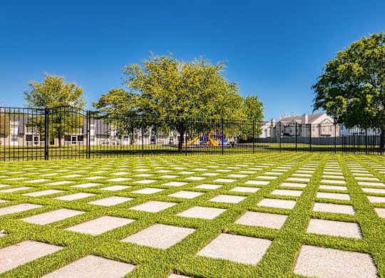 A park with a black fence and a green lawn with white rectangular stones.