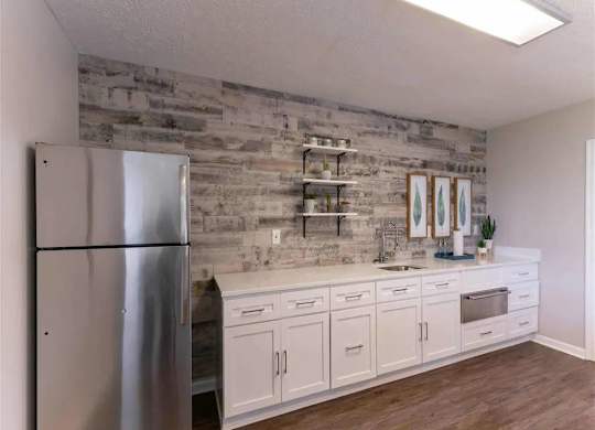 A kitchen with a refrigerator, cabinets, and a stone backsplash.