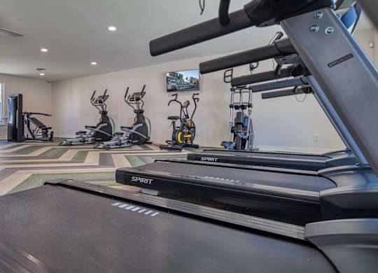 A treadmill in a gym with other exercise equipment.