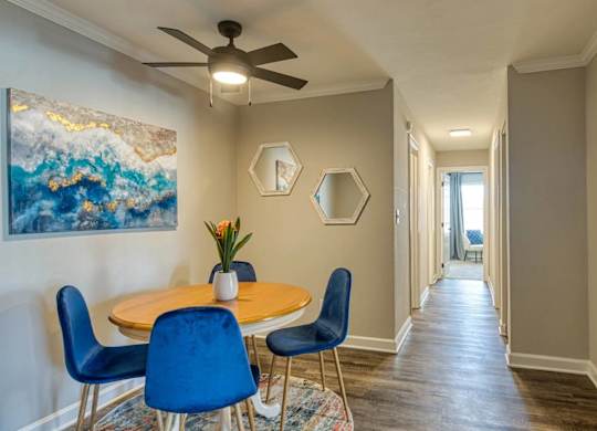 A dining room with a table and chairs and a painting on the wall.