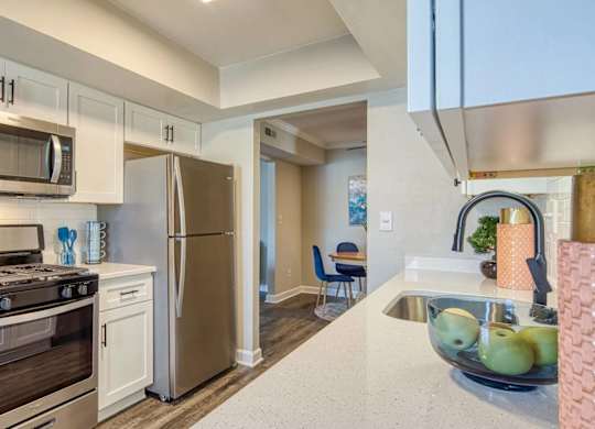 A kitchen with a stove, oven, refrigerator, and a bowl of fruit on the counter.