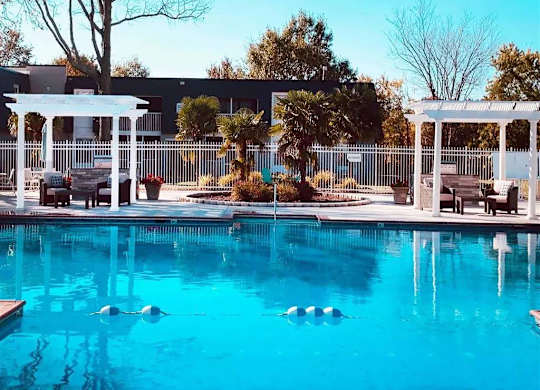 A pool with a white pergola and a fence in the background.