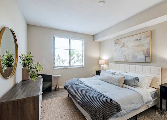 A bedroom with a large bed, a mirror, and a painting on the wall.