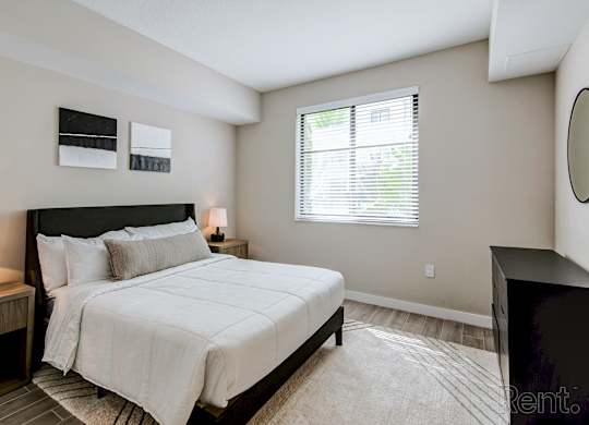A bedroom with a large bed and a window with blinds.