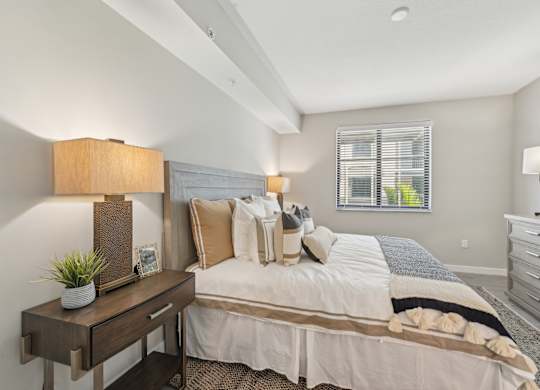 A well-lit bedroom with a large bed and a nightstand with a lamp.