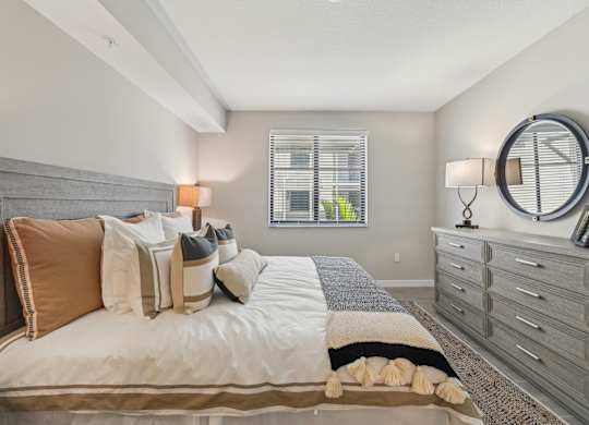 A bedroom with a bed, a dresser, and a window with blinds.