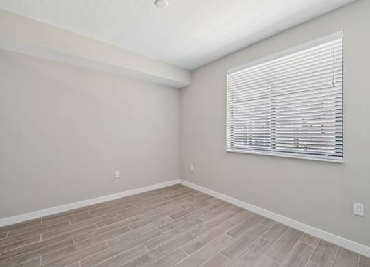 A room with a window covered by white blinds and wooden flooring.