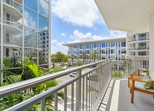 A balcony with a wooden chair and a table with a green cushion.