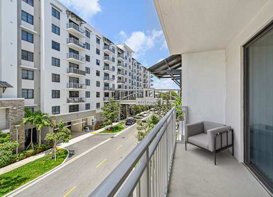 A balcony with a chair overlooks a street with apartment buildings.