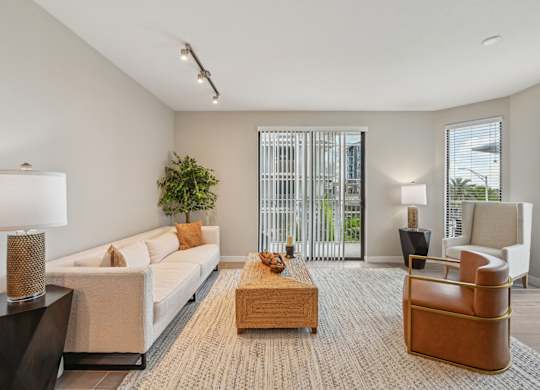 A living room with a white couch, a wooden coffee table, and a large window with a view of the outside.
