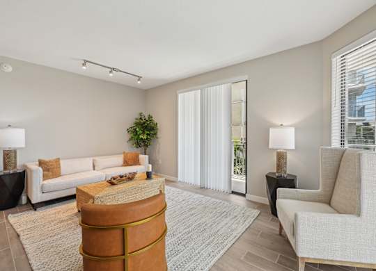 A living room with a white couch, a brown ottoman, and a grey rug.