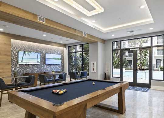 A pool table is in the middle of a room with a view of the outside.