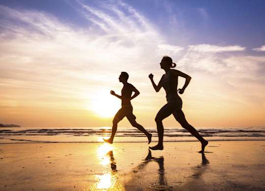 Two people running on the beach at sunset.