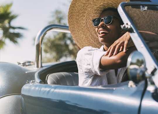 A person in a straw hat and sunglasses is driving a vintage car.