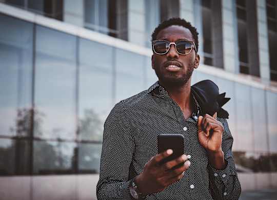 A man in a patterned shirt is holding a phone and adjusting his tie.