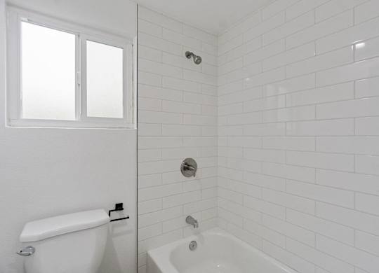 A white bathroom with a tub and toilet. at Torrance Gateway Apartments, Torrance, CA