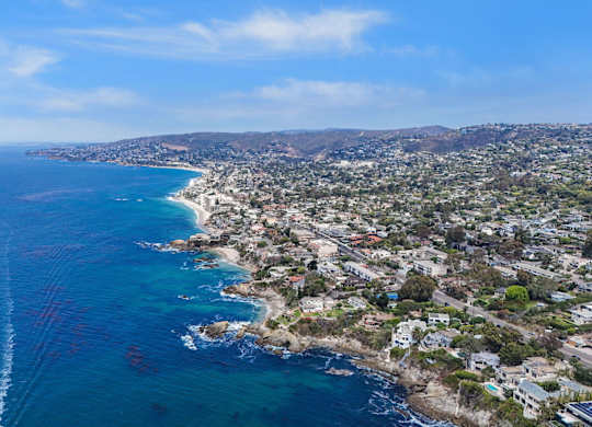 A coastal cityscape with a clear blue sky and a wake in the water from a boat.