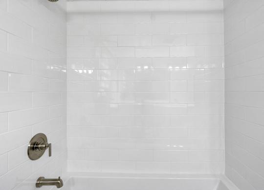 A white tiled shower with a silver faucet and a silver handle.