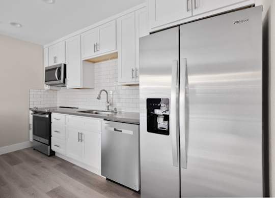 A modern kitchen with a stainless steel refrigerator and white cabinets.