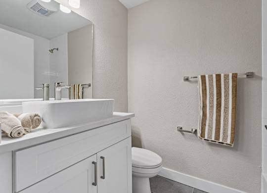 A white bathroom with a toilet, sink, and towel at Tamarack Sands Apartment Homes, California
