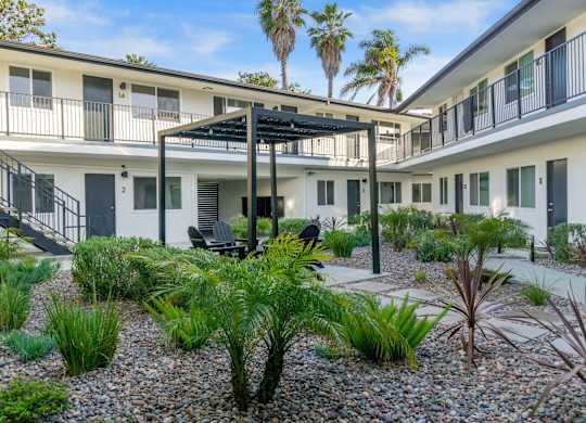 A patio area with a table and chairs surrounded by plants and trees. at Torrance Gateway Apartments, Torrance