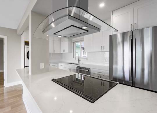 A modern kitchen with a stainless steel refrigerator and a black induction cooktop.