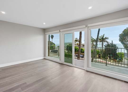 A room with a view of a street and palm trees through the glass doors.