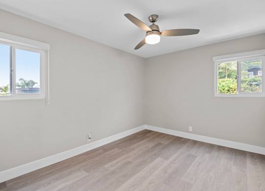 A room with a ceiling fan and two windows.