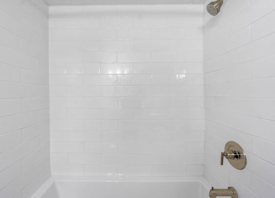 A white tiled shower with a shower head and faucet.