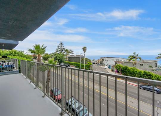 A view from a balcony overlooking a street with cars and houses.