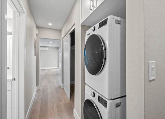 A white washing machine is stacked on top of another white washing machine in a narrow hallway.