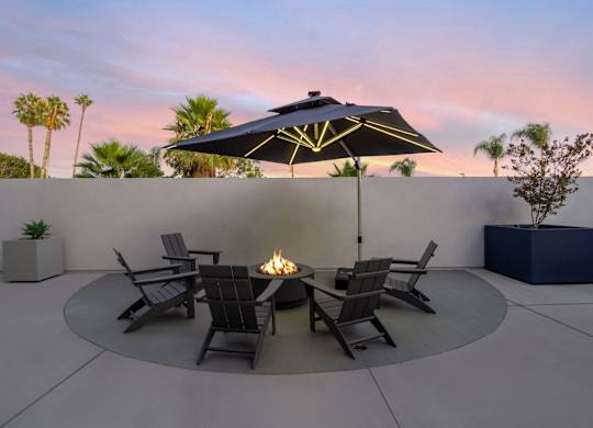 A patio with a fire pit and chairs under a black umbrella.at The Reserve La Mirada, La Mirada, California