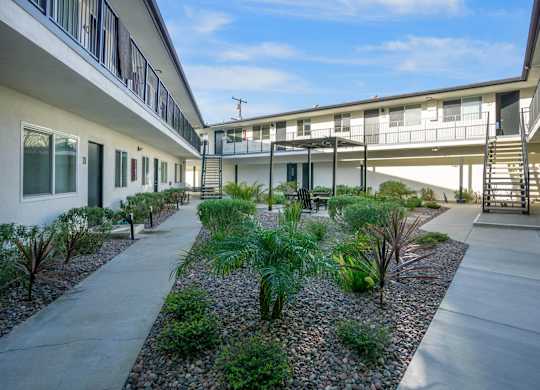 A concrete walkway leads between two buildings with a landscaped area in the middle. at Torrance Gateway Apartments, California, 90501