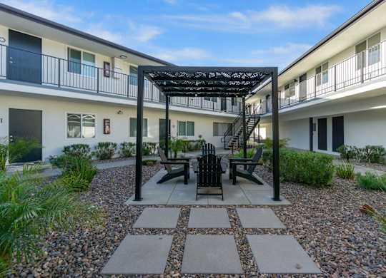 A patio with a table and chairs is surrounded by white buildings. at Torrance Gateway Apartments, Torrance, 90501