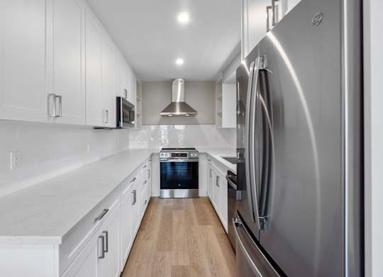A modern kitchen with a stainless steel refrigerator and wooden flooring.
