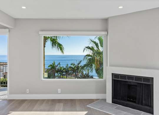 A modern living room with a fireplace and a view of the ocean through a large window.at Ocean Edge @ Laguna Beach, California