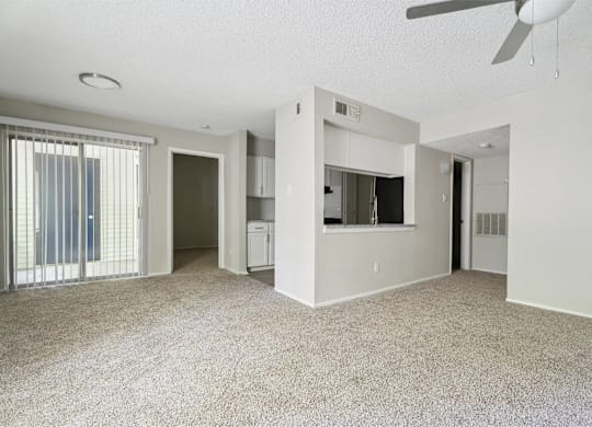A spacious living room with a ceiling fan and carpeted floor.
