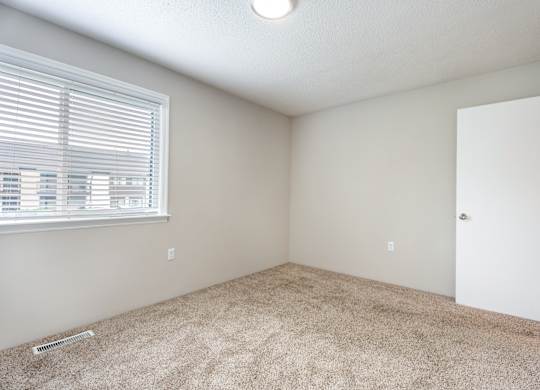 A room with a carpeted floor, a window with blinds, and a door.