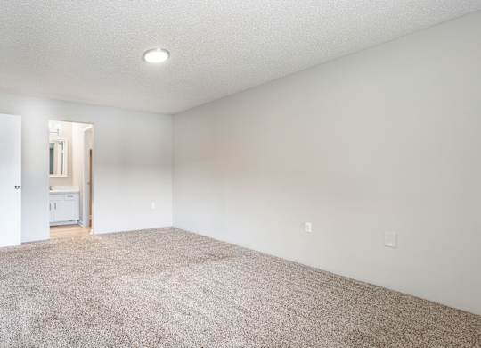 A large, empty room with a carpeted floor and a doorway leading to another room.