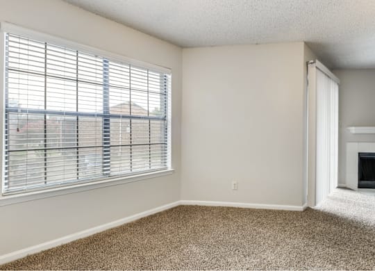 A room with a carpeted floor, a window with blinds, and a fireplace.