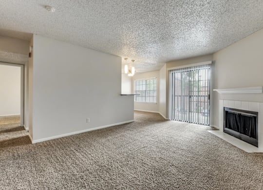 A sparsely furnished living room with a fireplace and a window with blinds.
