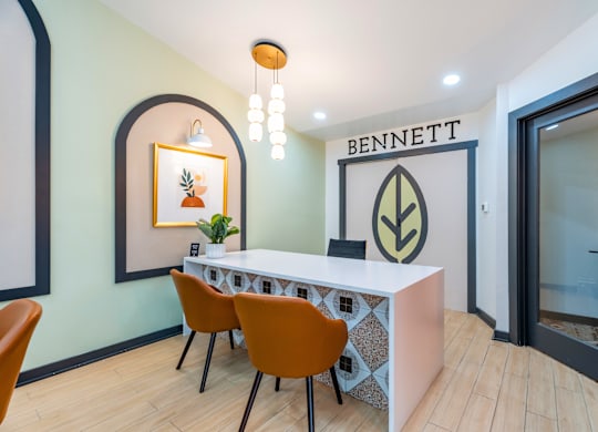 A reception area with a white desk and orange chairs.