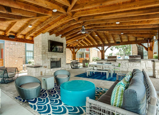 A large outdoor room with a stone fireplace and a blue and white rug.
