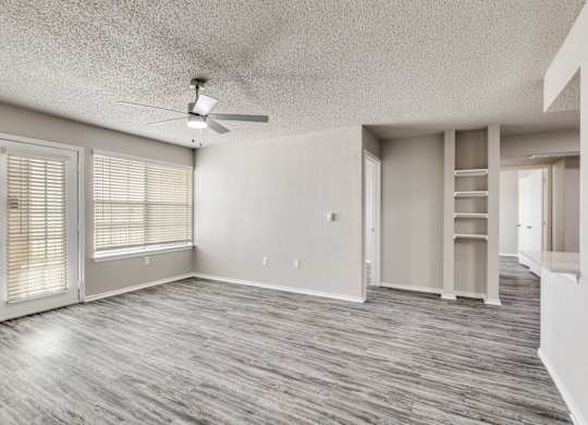 A spacious room with a ceiling fan and light, hardwood flooring, and a door with blinds.