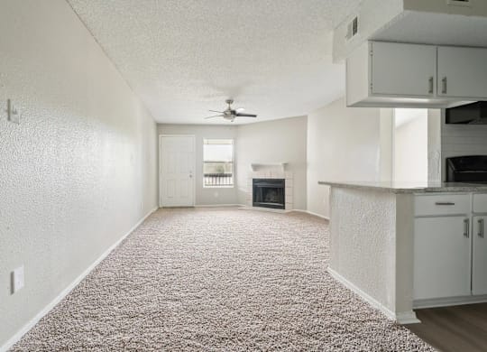 A sparsely furnished living room with a carpeted floor and a ceiling fan.