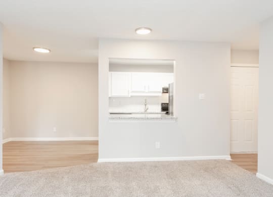 an empty living room with white walls and a white kitchen