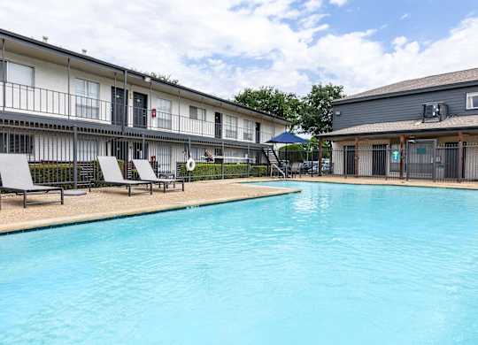 A swimming pool in front of a building with lounge chairs around it.